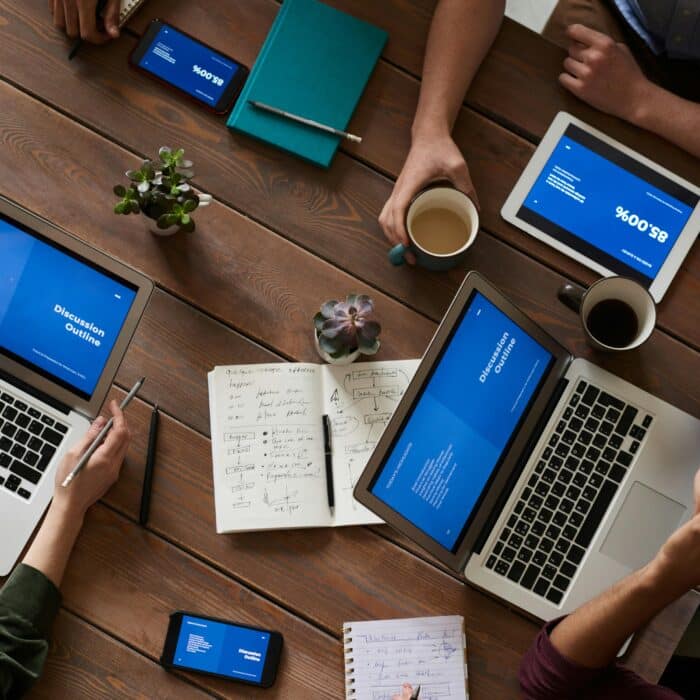 Top view of a diverse team using technology in a meeting. Laptops, tablets, and smartphones on a wooden table.